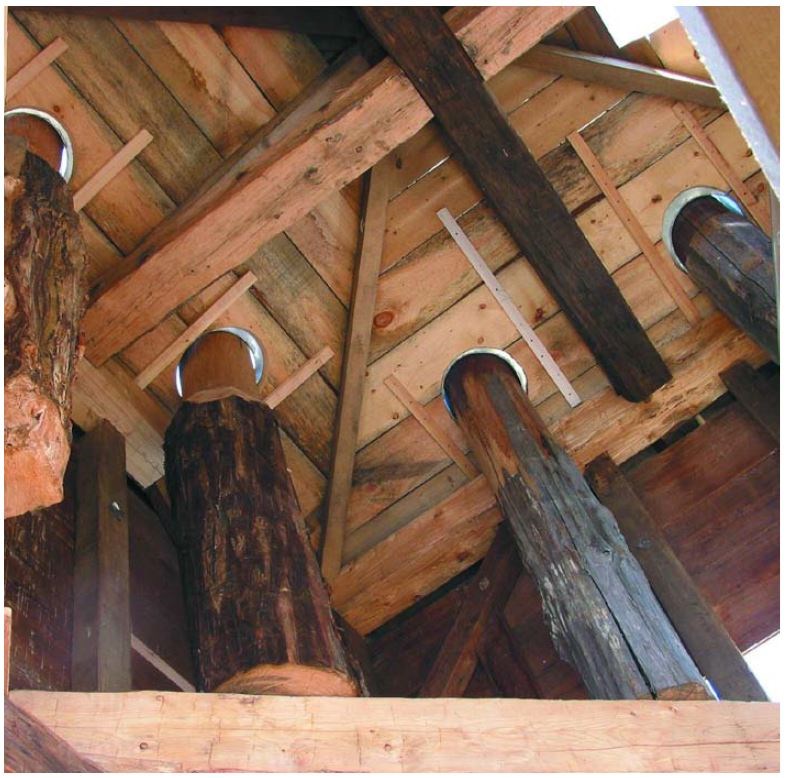 Looking up at three wooden posts supporting new thick timber decking and framing.