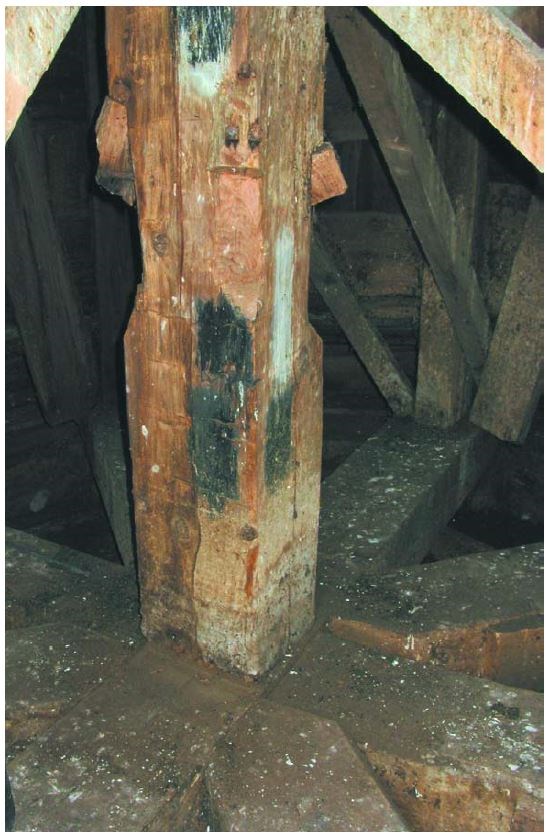 A thick square wooden center post with other framework in the background.