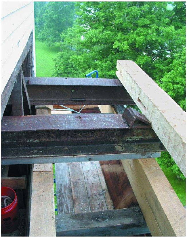 Two metal I-beams protrude from a wall are supported by timber beams.