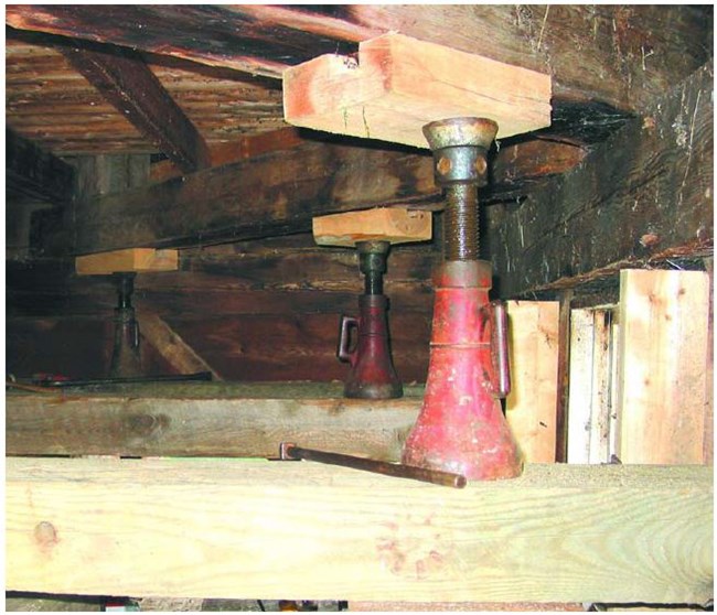 Three jackscrews with wooden blocks brace and support wooden decking.