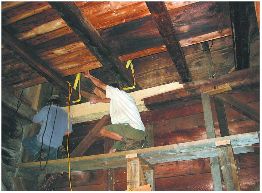 Two men kneeling wood plank scaffolding look at a new scarf joint.