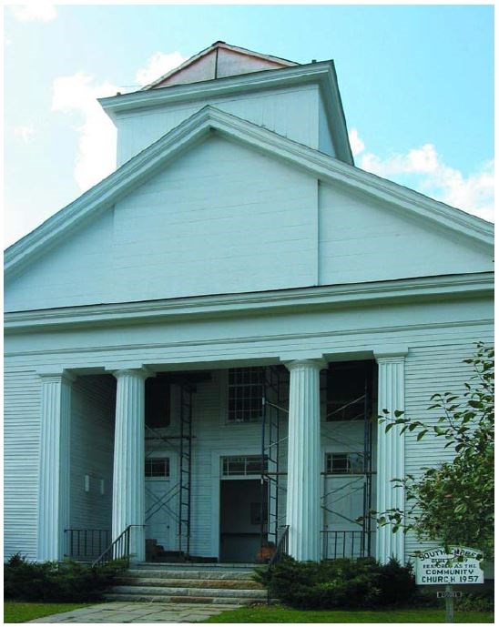 Weathered white Greek Revival façade of a church. Scaffolding is visible on both sides of the entrance.