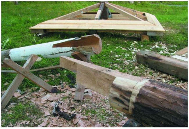 Two post being carved into a scarf  joint in the foreground and more framework in the background.