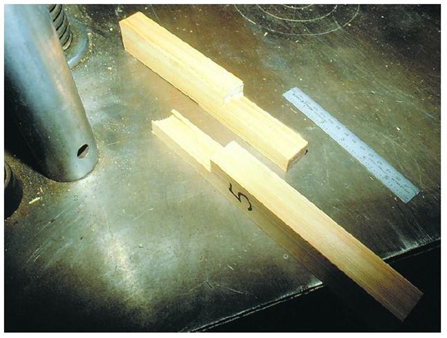 Two pieces of wood with notches cut out to form a joint next to a ruler.