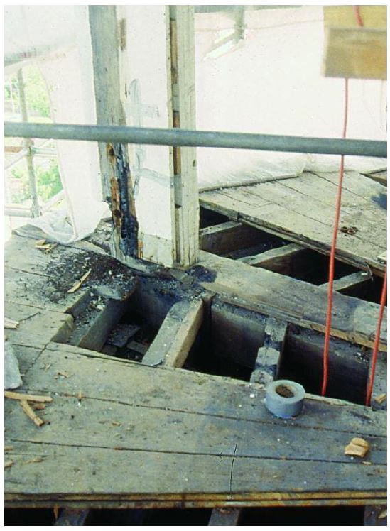 A decaying post rising out of a weathered deck with missing boards.