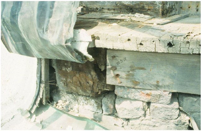Weathered decking sits on two deteriorating beams on a crumbling stone base.