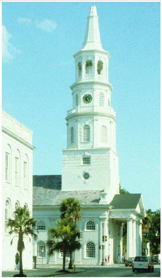 White steeple with belfry, clock, lantern, and spire on a white brick tower just behind the portico of a Greek revival church.