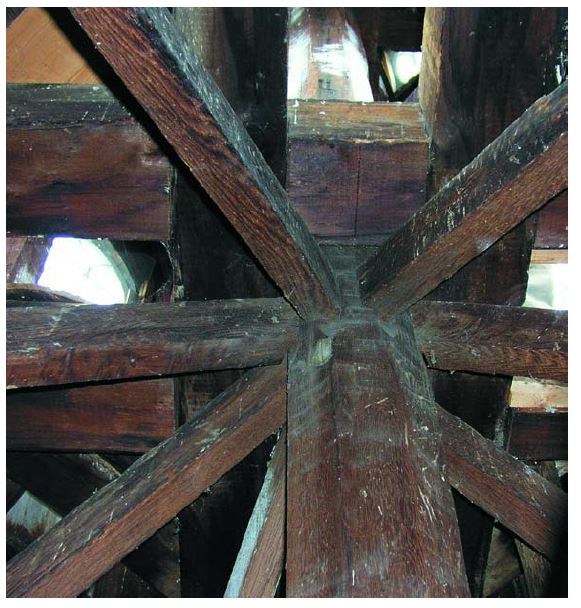 Eight timber beams join into a central post. Other timber beam framing visible in the background.