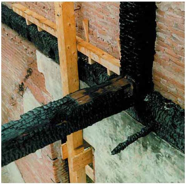 Heavily burnt timber beams stick out from a red brick wall.