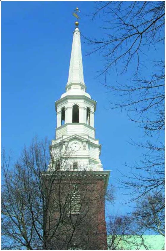 A white steeple with a lantern and spire with a weathervane stands on top of a red brick tower.