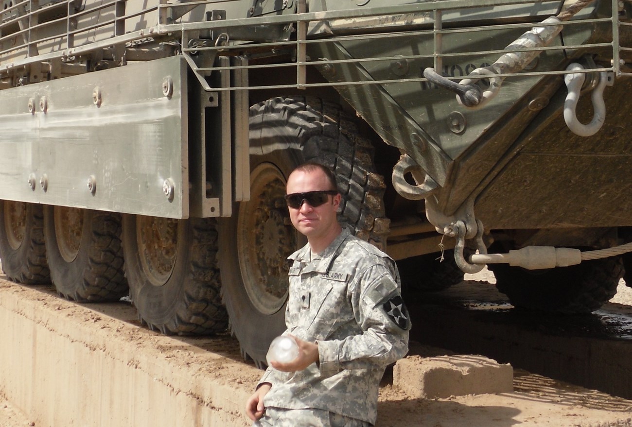 A modern uniformed soldier stands near a military vehicle.