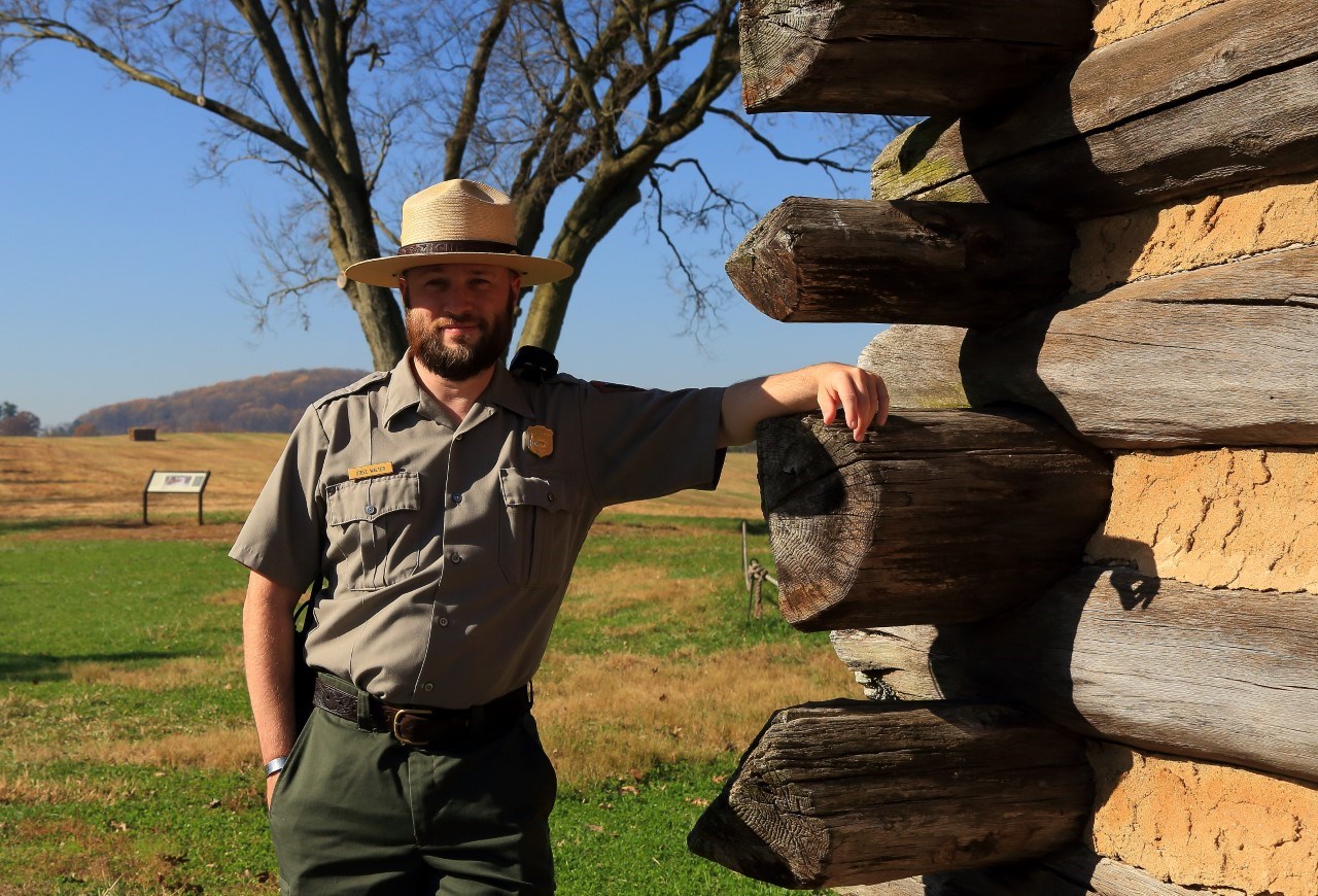 A park ranger stands in front of a wooden structure