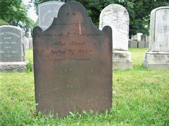 Reddish brown burial stone, with tripartite top, in a cemetery, green grass visible