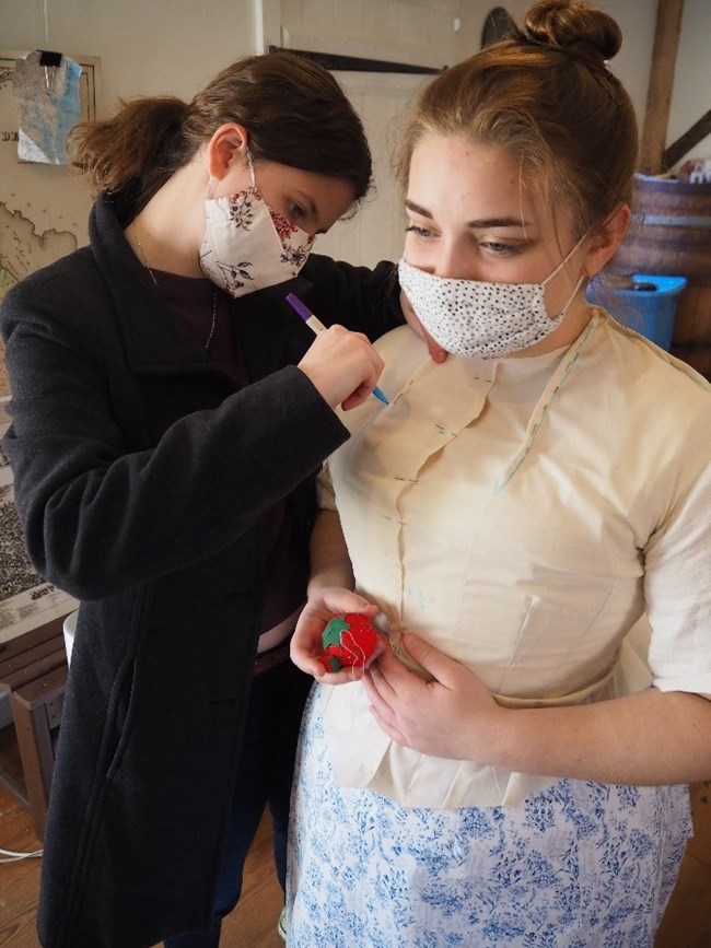 lt= A woman fits another woman for a Victorian dress.