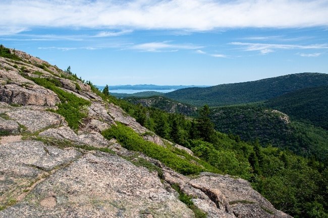 Sub Alpine Mountains A view from a granite mountain cliff overlooking a forest with mountains and water in the background