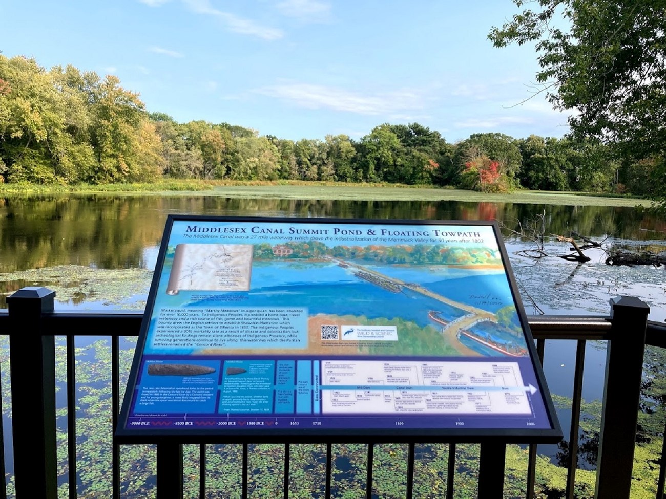 A colorful wayside titled "Middlesex Canal Summit Pond & Floating Towpath" displayed in front of a calm pond surrounded by trees
