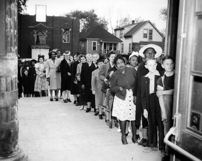 Black and white photo of men, women, and children of many ages and ethnicities in a long line.