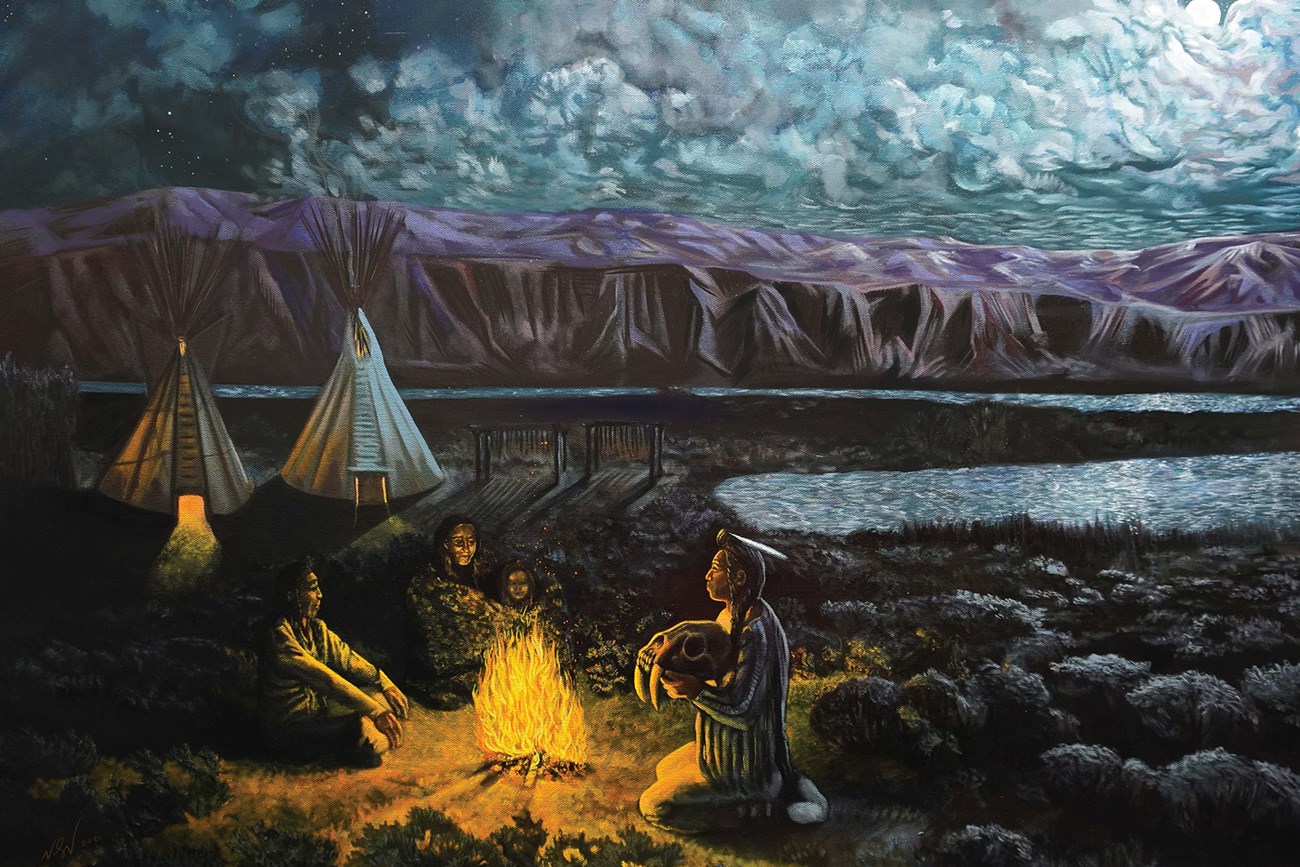 A painting of Shoshonean peoples gathered around a fire along the Snake River, lit by moonlight. One person holds the fossil skull of a saber-toothed cat. Behind the group are tipis and fish drying on racks.