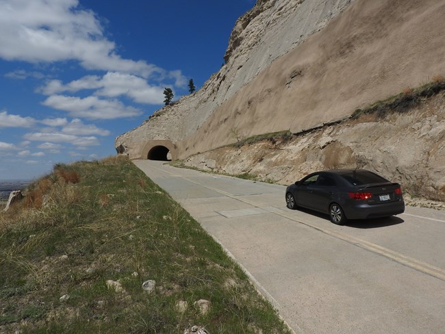 A car ascends a steep road, headed towards a tunnel.