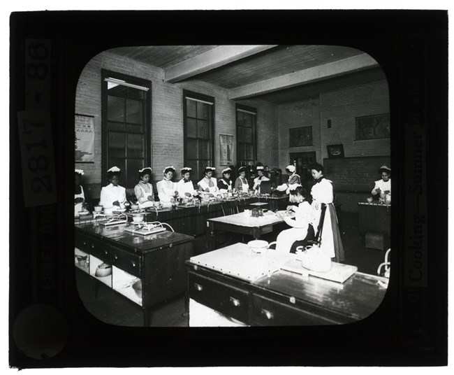 Large group of African American students attending a cooking class inside a high school in the 1880s.