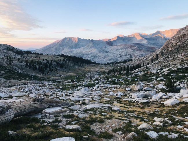 View of subalpine terrain scattered with boulders and morning light on distant peaks