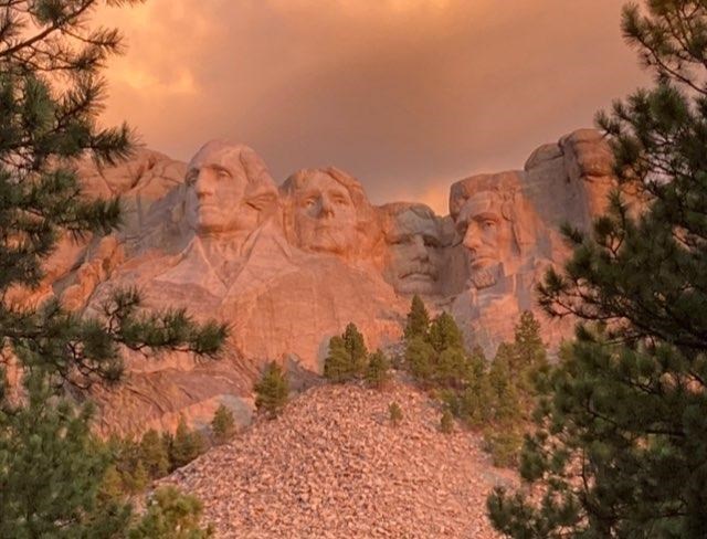 An early morning sunrise paints the Mount Rushmore sculpture in hues of pink, orange, yellow, and gray.