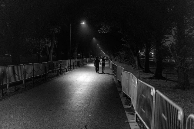 Barriers at the National Mall. July 2, 2019. A couple walks on a sparsely-lit park path lined with barriers at night.