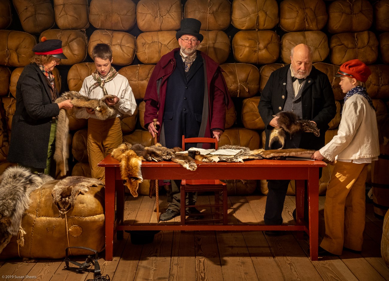 Six reenactors dressed in period clothing examine furs Six reenactors dressed in period clothing examine furs