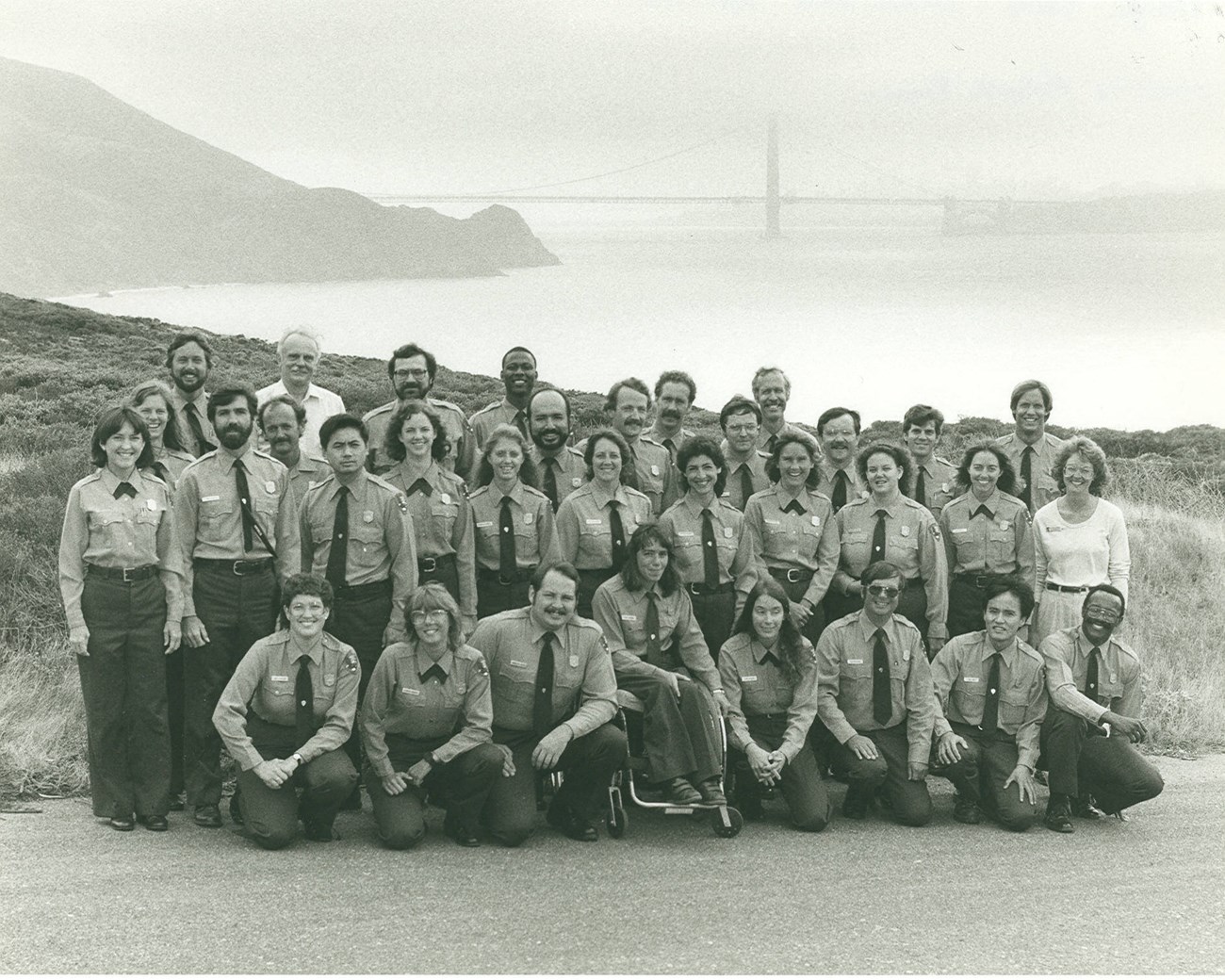 1984 Ranger Skills class photo Group of Park Service employees in uniform pose in four rows for a group photo with the Golden Gate Bridge in the distance.