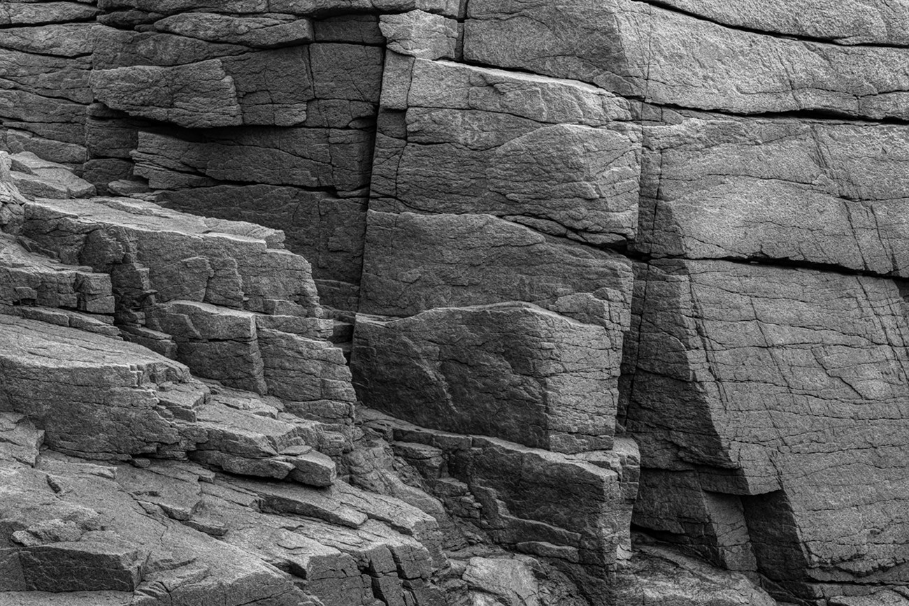Black and white study of light, shape, and fractures in a stone cliff face. Black and white study of light, shape, and fractures in a stone cliff face.