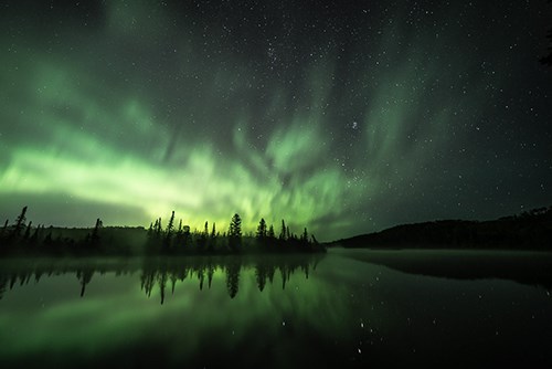 Glowing green aurora in a dark sky above a black horizon and reflection.