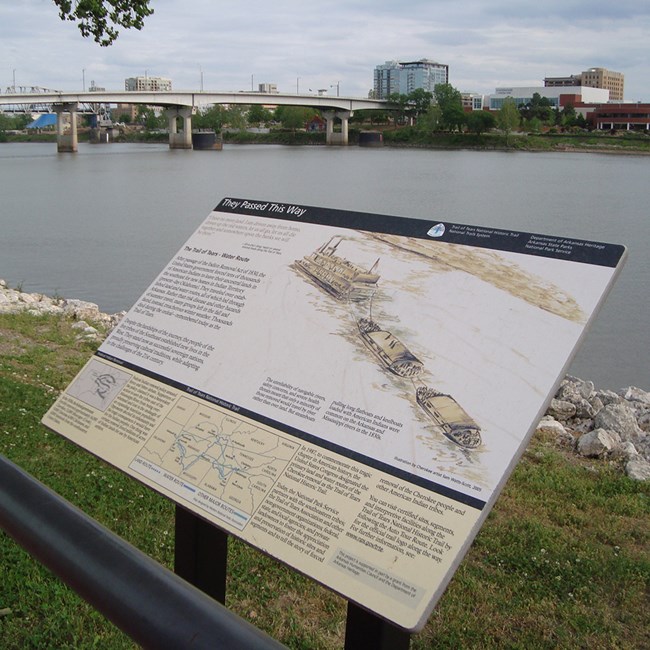 Exhibit along a waterfront with river, bridge, and city in the background.