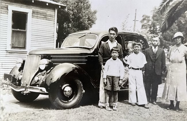TS family car Black and white photo of a family of six standing in front of a 1930s car