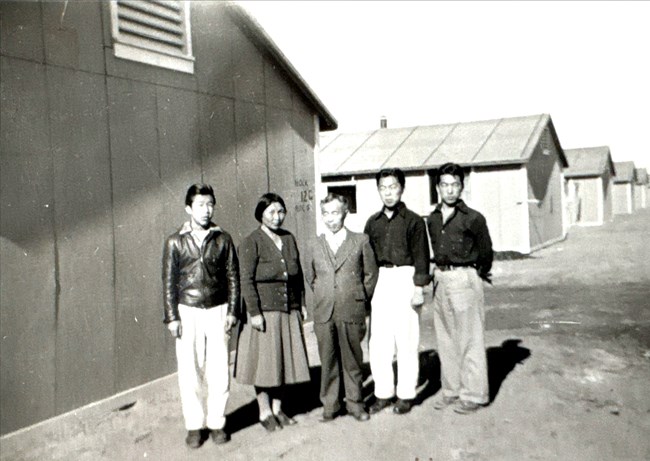 TS family Black and white photo of a family of five (four men, one woman) standing in front of a row of barracks.
