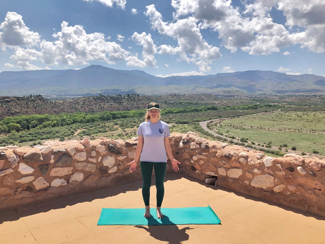 A smiling Park Ranger demonstrates mountain pose at the top of Tuzigoot Pueblo. A smiling Park Ranger demonstrates mountain pose at the top of Tuzigoot Pueblo.