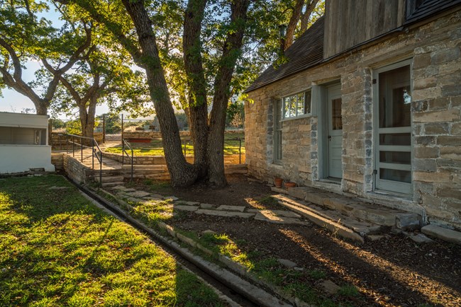 The front yard of the Frijole Ranch house A stone house is fronted by a yard with a small channel of water flowing through it