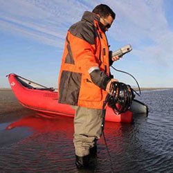 Picture of Tahzay Jones standing in ankle-deep water taking readings with an instrument.