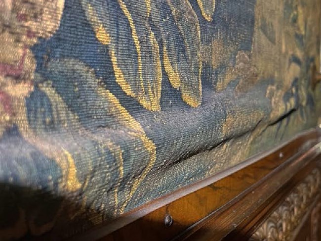 Detail of a tapestry with heavy dust accumulation on top of slumping areas.