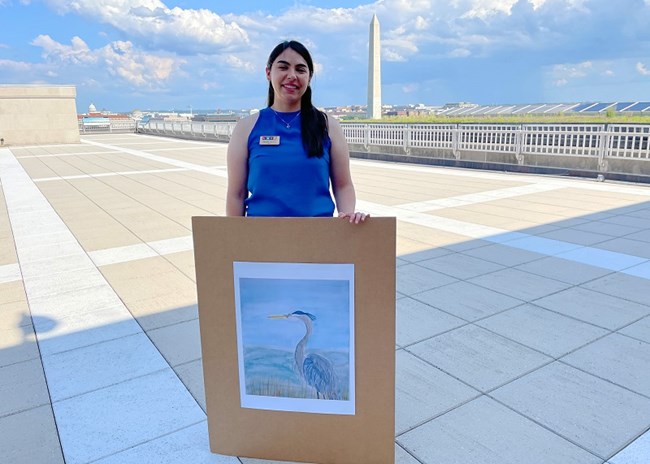 Tatiana Mihaita person holding a painting of a bird, with the Washington Monument in the background