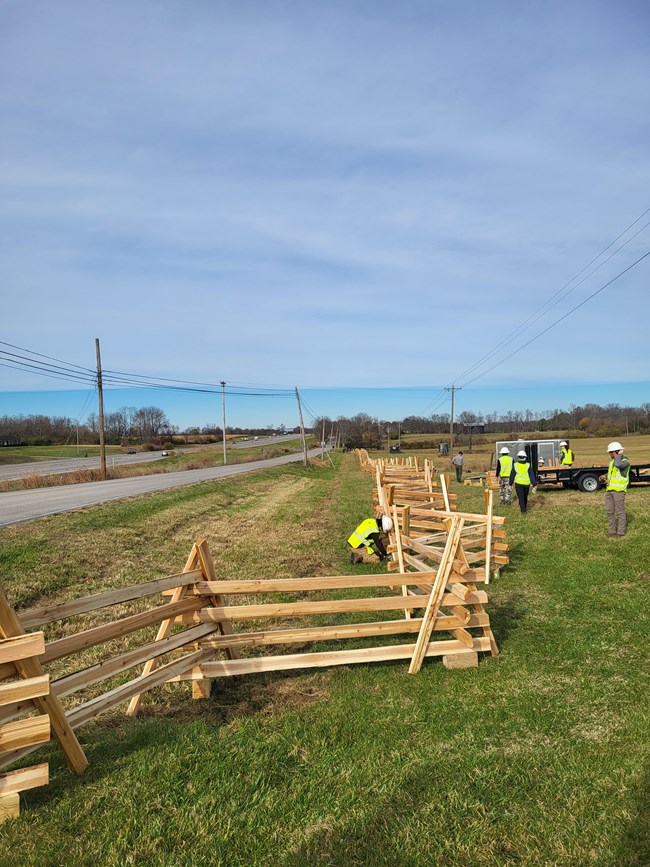 Team standing in a field unloading split-rail fence pieces from trailer.