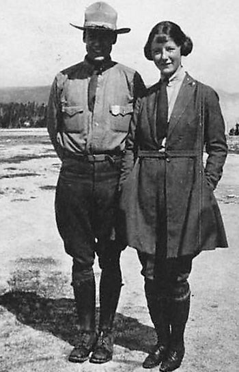 Marguerite Lindsley wears the NPS prescribed temporary ranger uniform and stands next to a man in NPS uniform.