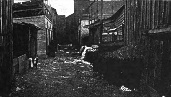 View of a Chicago Tenement Alley, unpaved, muddy, and full of trash