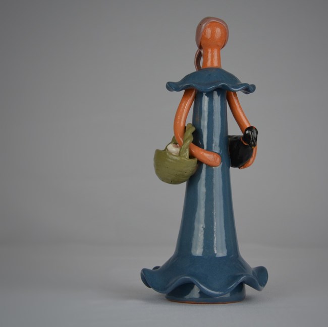 Dominican Faceless Doll Ceramic faceless doll wearing a blue dress holding a green basket and black chicken.