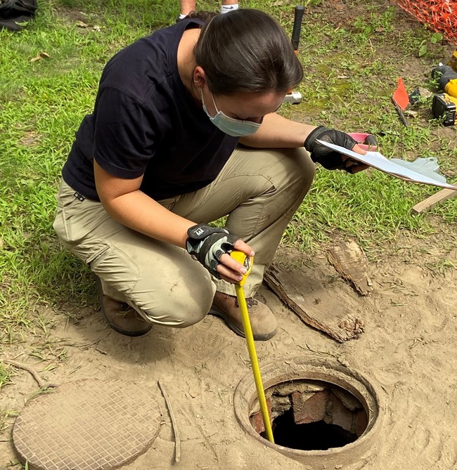 Person puts a measuring tape into a hole in the ground.