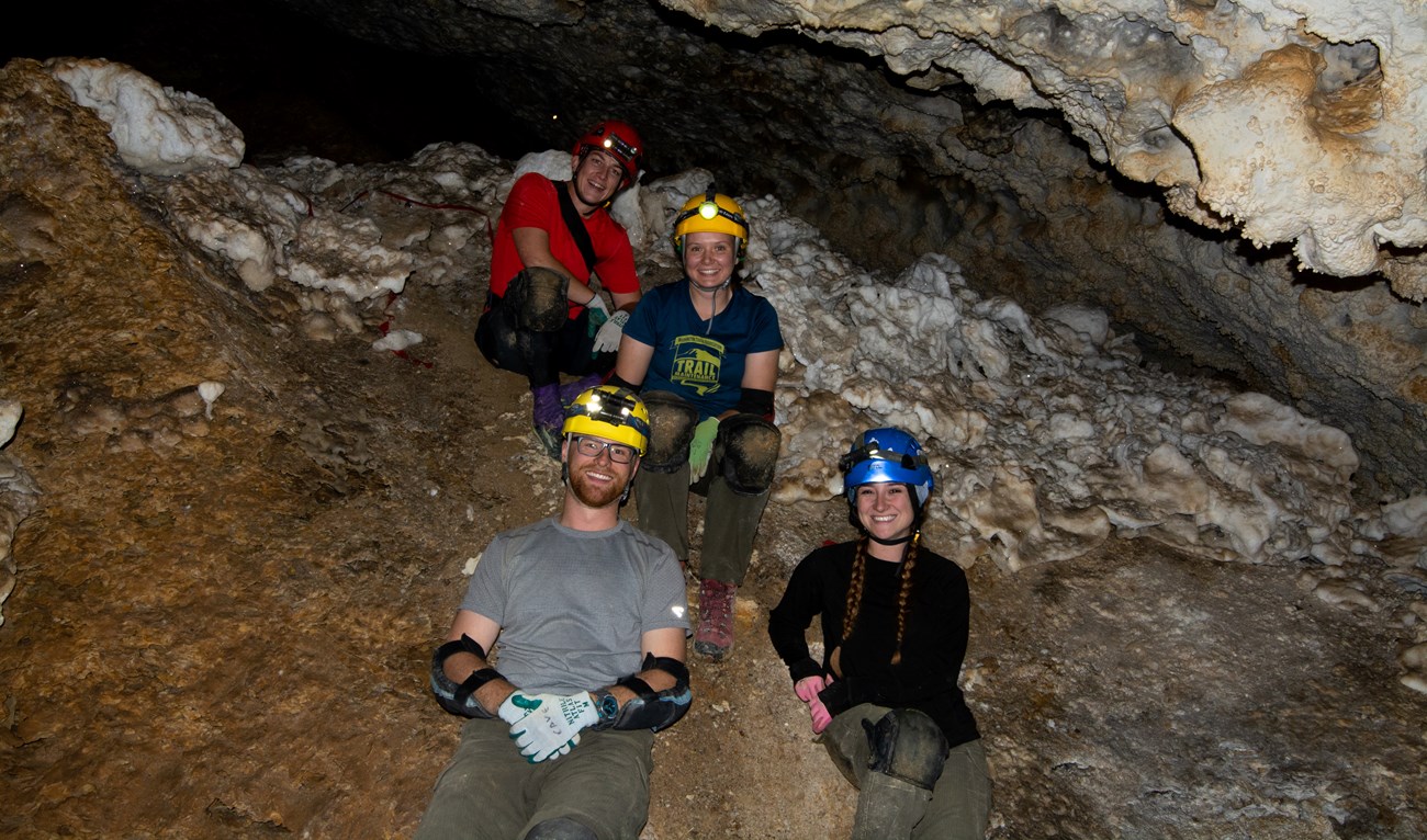 group of four cavers wearing helmets in a cave