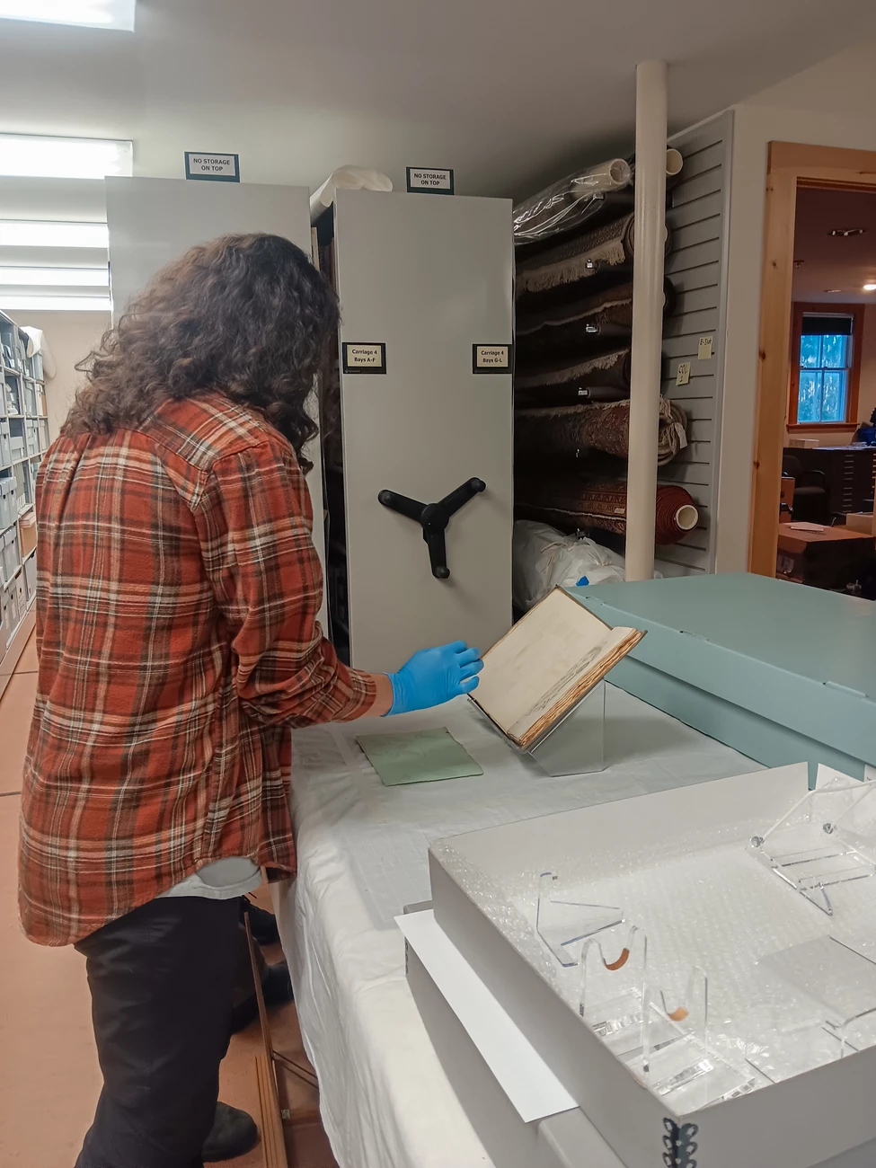 Tiffany in Collections person wearing blue curatorial gloves carefully examines a historical book in the park archives