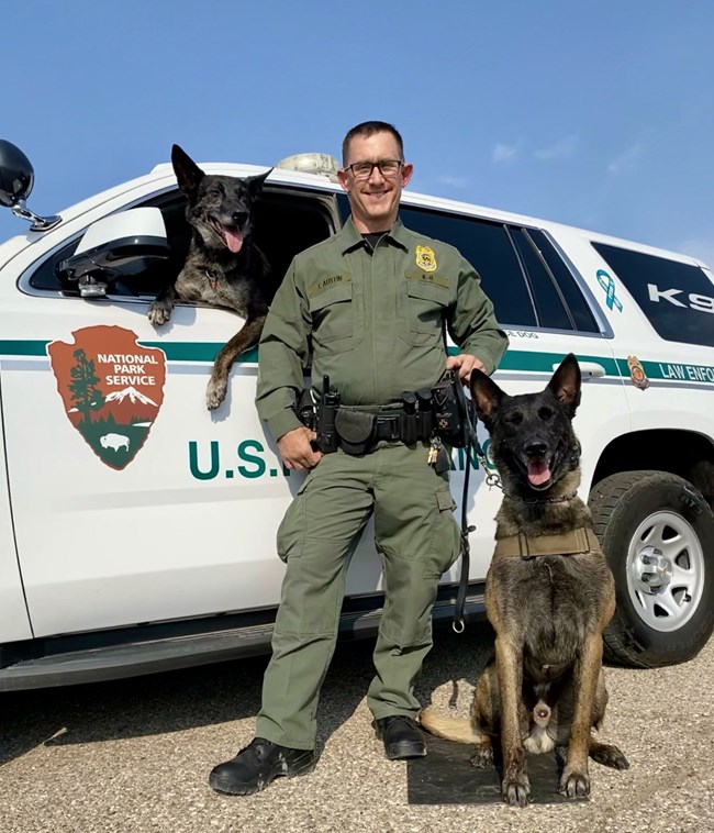 Ranger Todd Austin standing next to a ranger vehicle with two canines