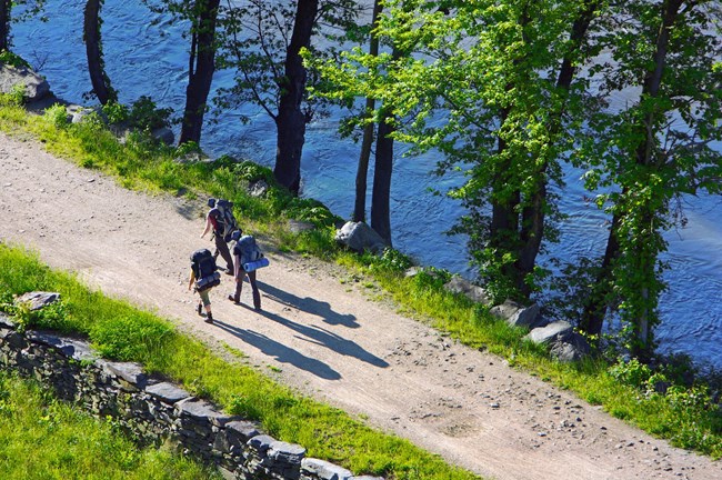 Three hikers with backpacks and bedrolls walk on the towpath.