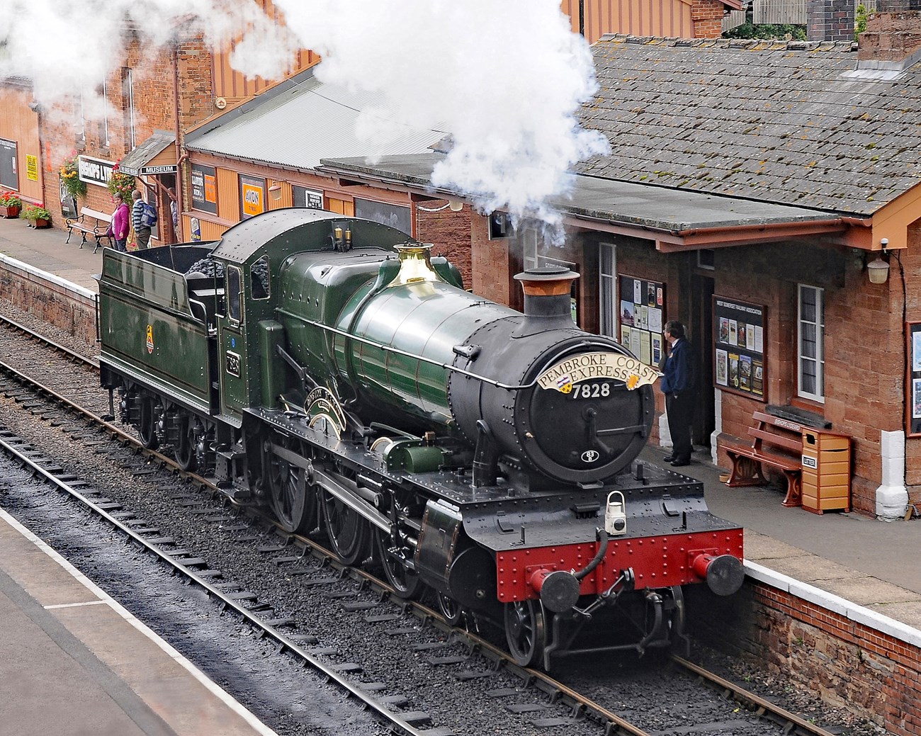 Train - Terence Burke Green and red train with smoke blowing out of it stopping at a train station.