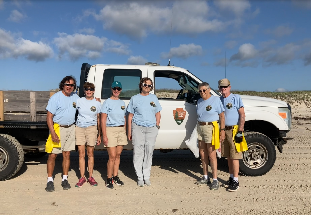 Trashbusters A group of people wearing matching shirts stand next to a white truck parked on a beach.